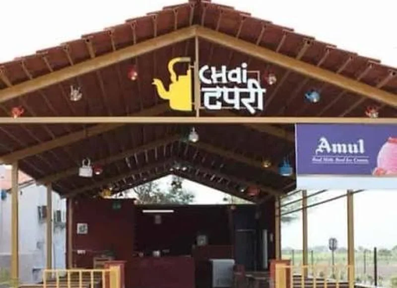 Roadside chai tapri with a tiled roof, a yellow teapot sign and hanging kettles